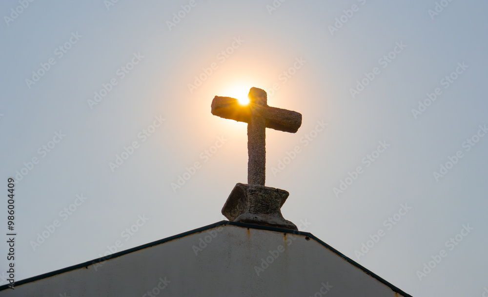 Sun rising behind stone cross on an old, historic Catholic church in rural Portugal, in the early morning. Close up. Sun rising behind stone cross on an old, historic Catholic church in rural Portugal, in the early morning. Close up.