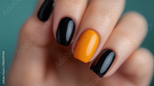 A close-up of a hand showcasing a manicure with glossy orange and black nails, reflecting a bold and stylish fashion statement suitable for modern trends and aesthetics. photo