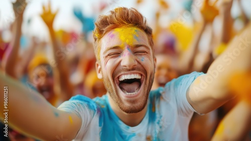 A cheerful man covered in vibrant colors laughs wholeheartedly amidst a lively festival crowd, highlighting the energy and joy of a cultural celebration outdoors. photo