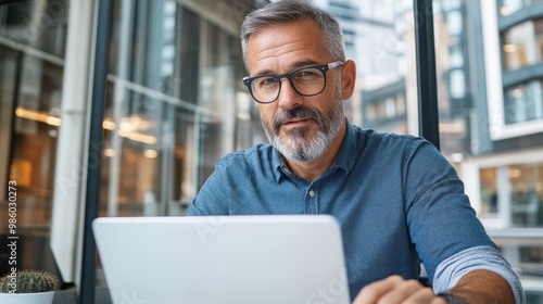 Handsome gray-haired man intently looking at a laptop, surrounded by an urban environment that offers a blend of sophistication and technology-driven atmosphere.