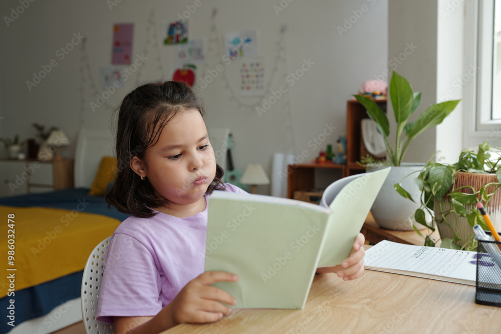Tired schoolgirl sitting at her desk and reading textbook Tired schoolgirl sitting at her desk and reading textbook