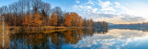 Beautiful autumn trees with leaves in vibrant hues reflect perfectly off the calm lake water under a bright blue sky.