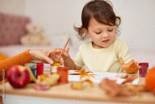 smiling little child girl painting her hands and autumn leaves. baby girl drawing hands in yellow paint photo