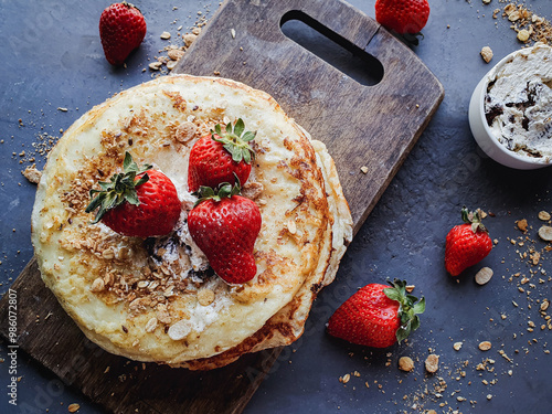 Pancakes with cream and strawberries on wooden board and dark rustic background