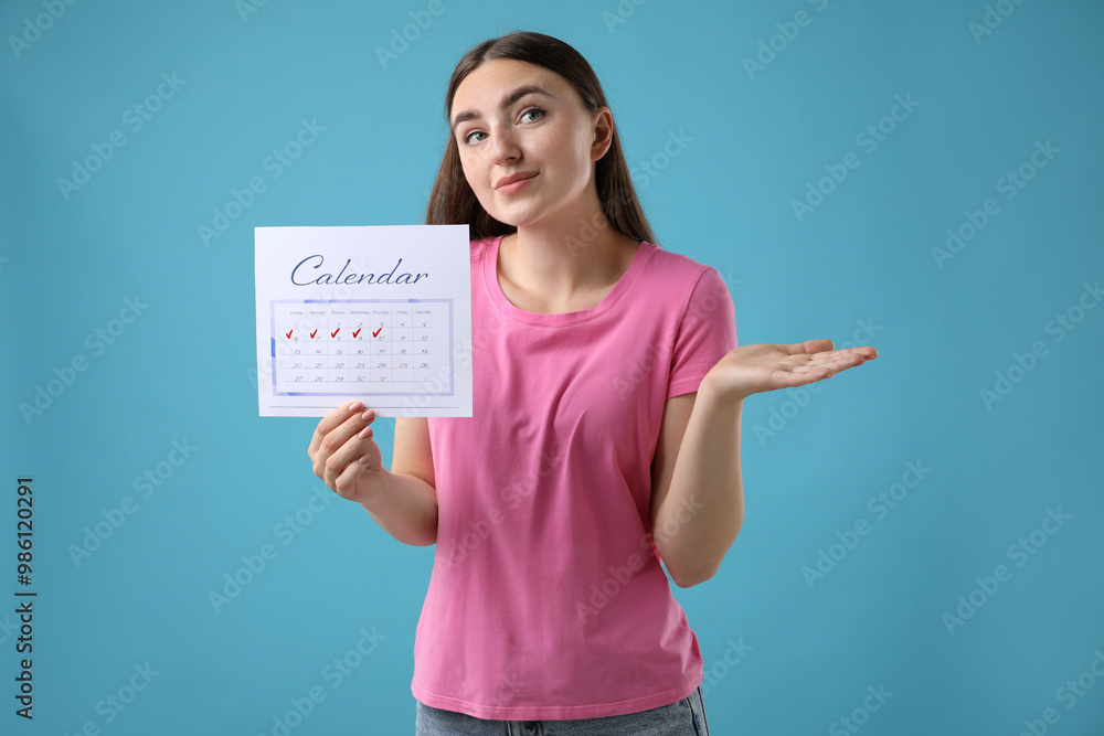 Woman holding calendar with marked menstrual cycle days on light blue background Woman holding calendar with marked menstrual cycle days on light blue background