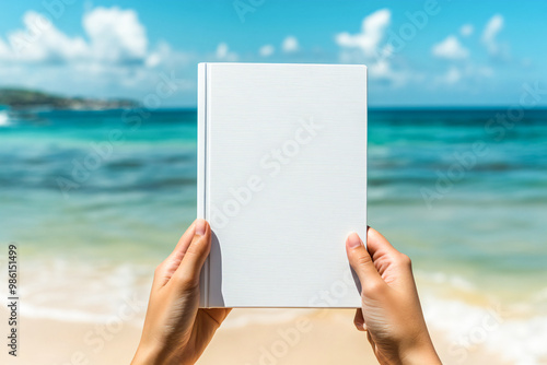 People hands holding a white book mockup with copy space in front of a beautiful beach