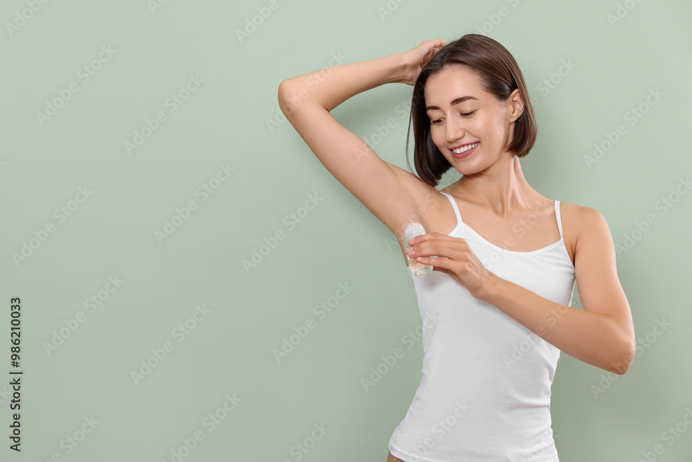 Smiling woman applying roll-on deodorant on green background. Space for text Smiling woman applying roll-on deodorant on green background. Space for text