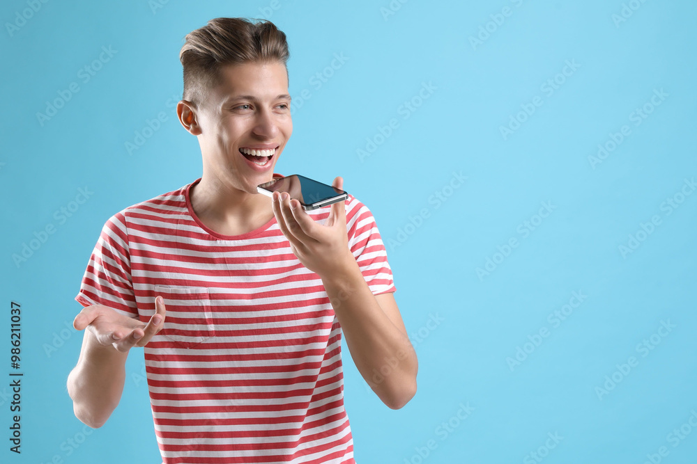 Young man recording voice message via smartphone on light blue background, space for text Young man recording voice message via smartphone on light blue background, space for text