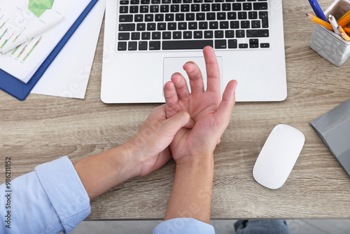 Canvastavla Man suffering from pain in wrist while working on laptop at wooden table, closeup, top view