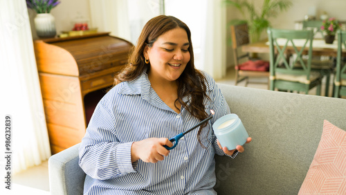 Bild auf Leinwand Smiling young woman with a plus size figure sits on her couch, lighting a scente