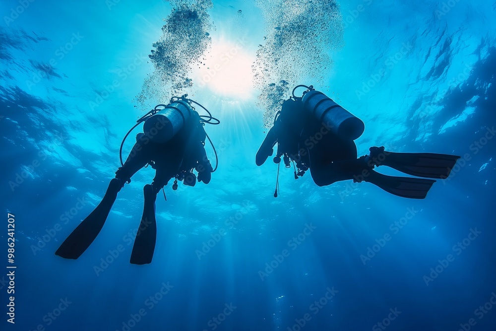 Two divers exploring the underwater world, surrounded by sunlight, in clear blue ocean waters during a scenic day Two divers exploring the underwater world, surrounded by sunlight, in clear blue ocean waters during a scenic day