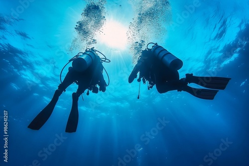 Two divers exploring the underwater world, surrounded by sunlight, in clear blue ocean waters during a scenic day