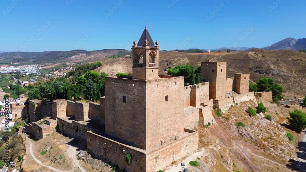Drone flight around the Alcazaba fortress of Antequera, Spain located on a hill and surrounded by historic town with typical andalusian white houses and old churches. Mountains in the background. Drone flight around the Alcazaba fortress of Antequera, Spain located on a hill and surrounded by historic town with typical andalusian white houses and old churches. Mountains in the background.