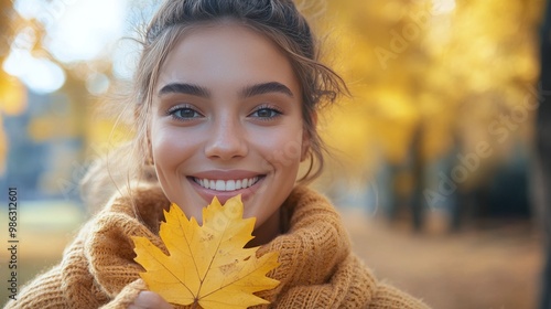 Young woman joyfully holding a yellow maple leaf during autumn in a park on a...