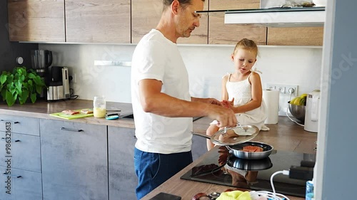 Young father and daughter cooking fish with stove and frying pan together in home kitchen photo