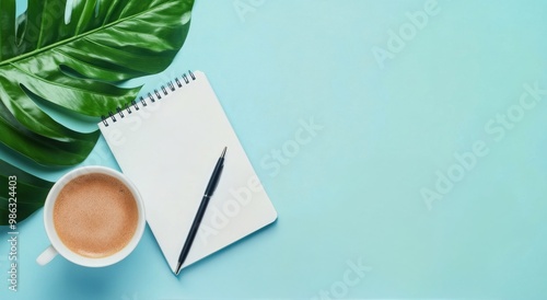 A cozy workspace featuring a coffee cup, a notepad, and a green leaf on a lig...