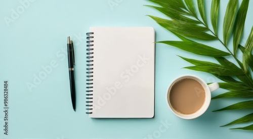 A cozy workspace featuring a coffee cup, a notepad, and a green leaf on a lig...