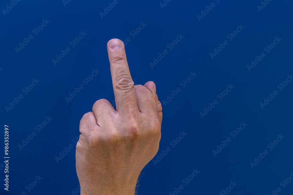 Hand showing offensive fuck you symbol on blue background Hand showing offensive fuck you symbol on blue background