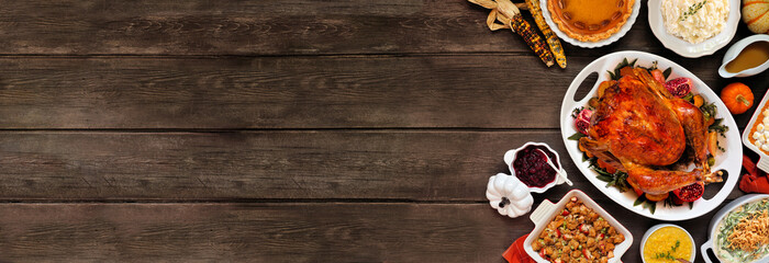 Traditional Thanksgiving turkey dinner. Overhead view side border on a rustic dark wood banner background. Turkey, mashed potatoes, stuffing, casseroles, pumpkin pie and sides.