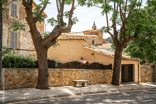 Straße mit Fußgängerweg und einer Sitzbank zwischen zwei Bäumen vor einer Steinmauer in Valldemossa auf der spanischen Baleareninsel Mallorca  photo