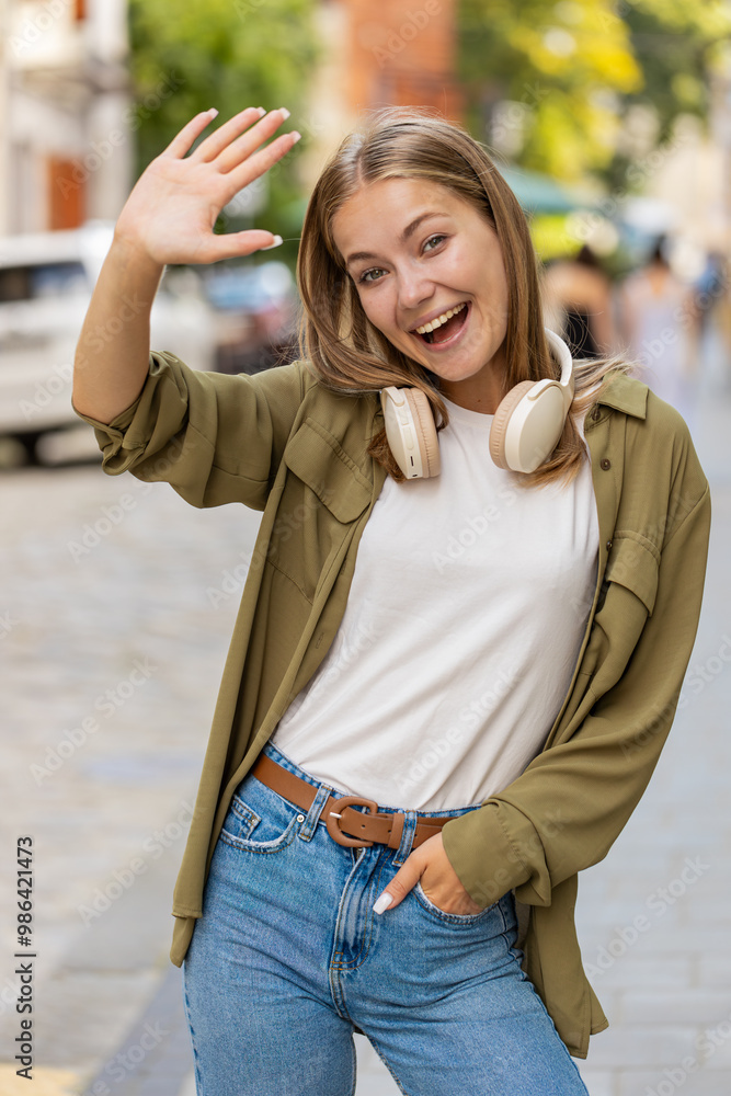 Hello. Caucasian young woman smiling friendly at camera, waving hands gesturing hi, greeting or goodbye, welcoming with hospitable expression outdoors. Happy girl on city street. Lifestyles. Vertical Hello. Caucasian young woman smiling friendly at camera, waving hands gesturing hi, greeting or goodbye, welcoming with hospitable expression outdoors. Happy girl on city street. Lifestyles. Vertical