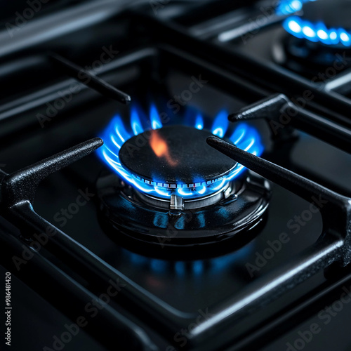 Gas burner with a blue flame on a black kitchen stove, with a cast-iron grate, top view, selective soft focus. gas crisis.