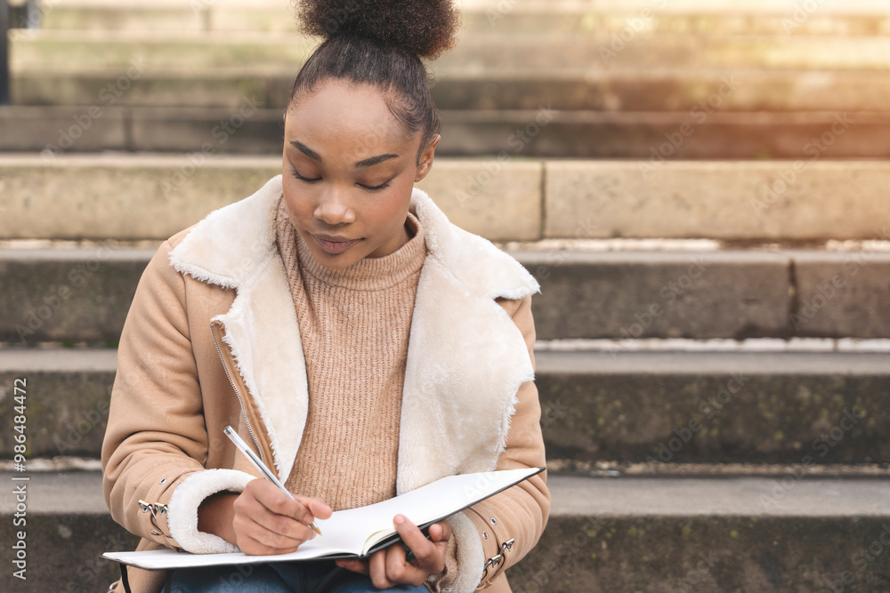 Fototapeta premium Young Woman Creatively Journaling on Stone Steps in Quiet Urban Setting During Daylight