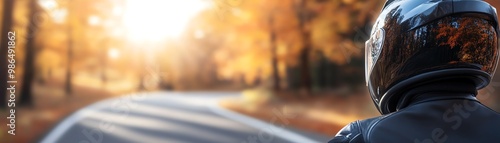 Motorcyclist on scenic autumn road, surrounded by vibrant fall foliage and sunlight creating a peaceful and adventurous atmosphere.