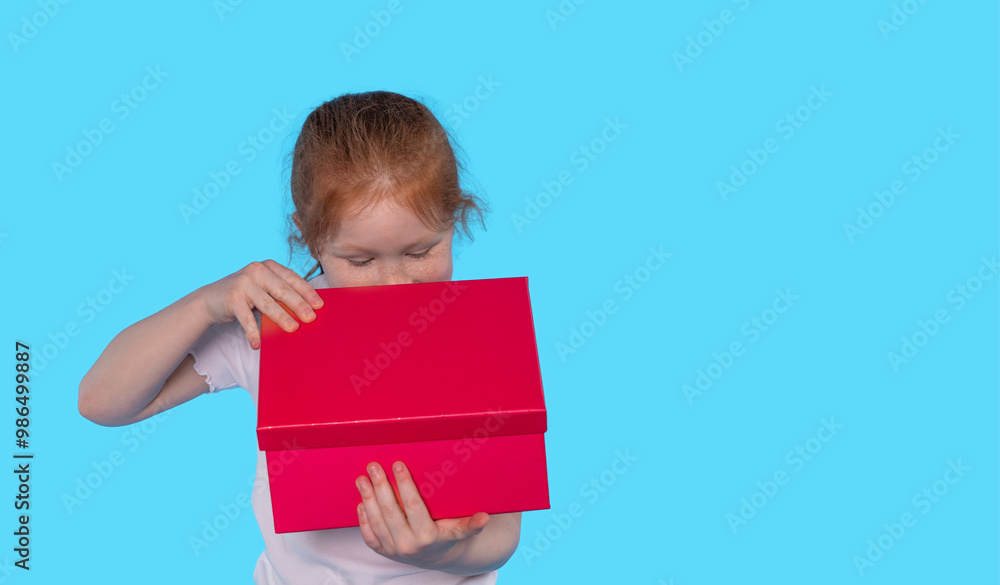 Curious Child Exploring Bright Red Gift Box Against Vibrant Blue Background Curious Child Exploring Bright Red Gift Box Against Vibrant Blue Background