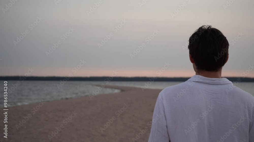 a man in a white shirt walks along a sandy spit near the sea at a red-pink sunset a man in a white shirt walks along a sandy spit near the sea at a red-pink sunset