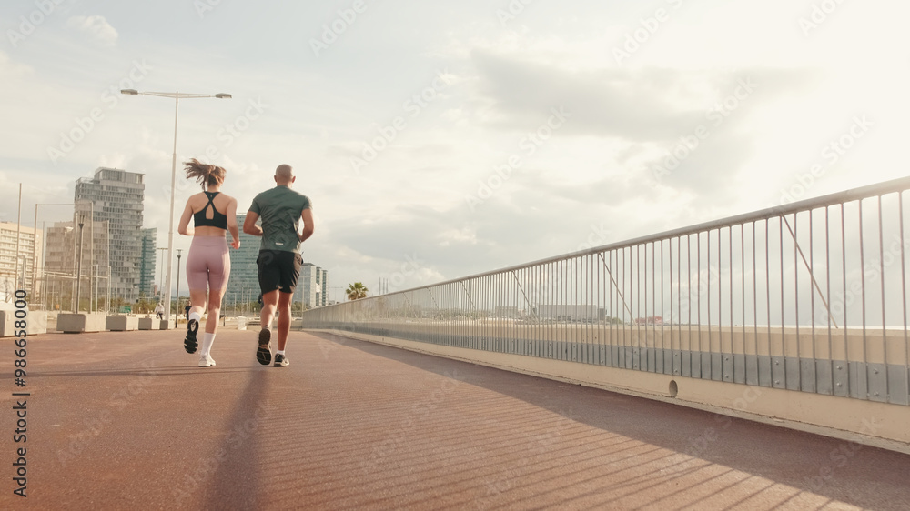 Panorama view of seafront, young active couple jogging together along the beach, Back view Panorama view of seafront, young active couple jogging together along the beach, Back view