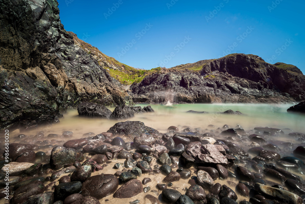 A rocky beach in Cornwall, England, with dark, dramatic rocks leading to a secluded cove with turquoise water under a vibrant blue sky, creates a captivating scene of coastal beauty. A rocky beach in Cornwall, England, with dark, dramatic rocks leading to a secluded cove with turquoise water under a vibrant blue sky, creates a captivating scene of coastal beauty.