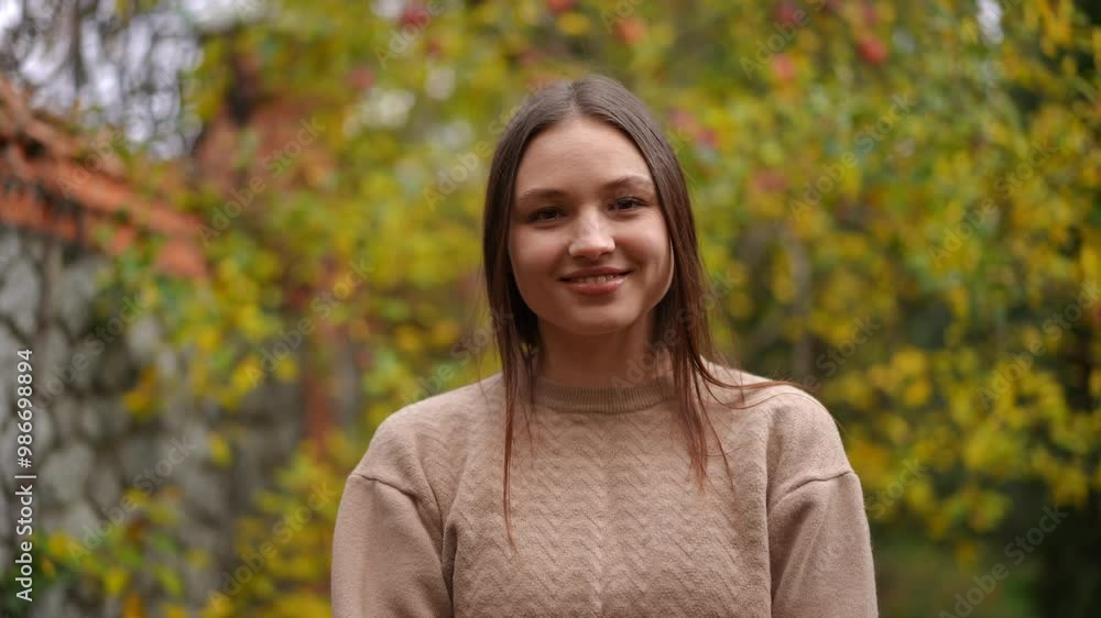 A cheerful young woman stands gracefully in a vibrant autumn garden, surrounded by colorful foliage A cheerful young woman stands gracefully in a vibrant autumn garden, surrounded by colorful foliage