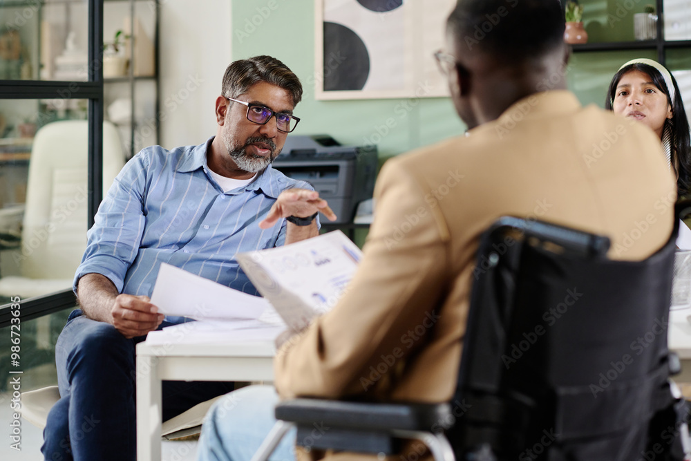 Diverse group of professionals discussing documents in modern office environment, with Caucasian man leading conversation and African American man taking notes Diverse group of professionals discussing documents in modern office environment, with Caucasian man leading conversation and African American man taking notes