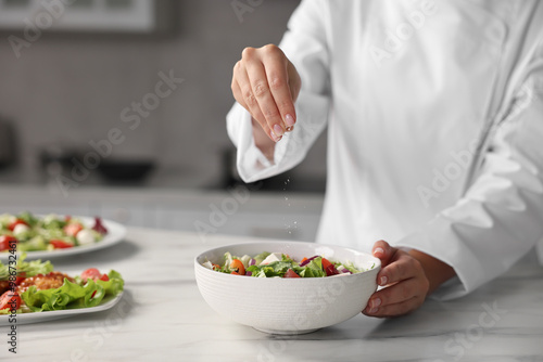 Professional chef adding salt to delicious salad at white marble table in kitchen, closeup