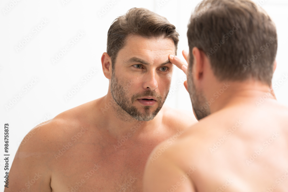 sexy man with stubble looks at the wrinkles on his face. Close up man looking in mirror, sensitive skin, cosmetology treatment. Skin care. joyful, virile, manly, attractive, naked, unshaven, handsome sexy man with stubble looks at the wrinkles on his face. Close up man looking in mirror, sensitive skin, cosmetology treatment. Skin care. joyful, virile, manly, attractive, naked, unshaven, handsome