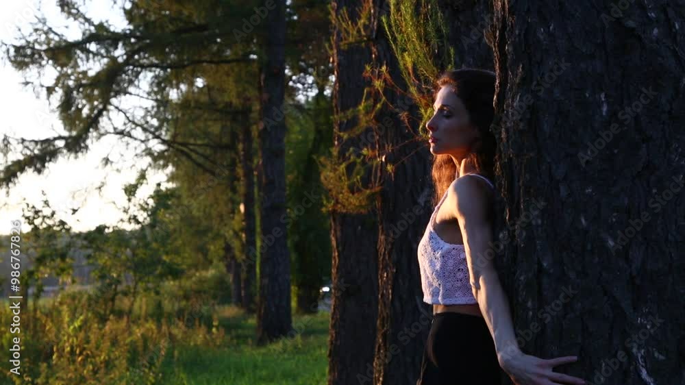 Beautiful happy woman enjoing good warm autumn weather on sunset background in fashion clothes near the tree in the park Beautiful happy woman enjoing good warm autumn weather on sunset background in fashion clothes near the tree in the park