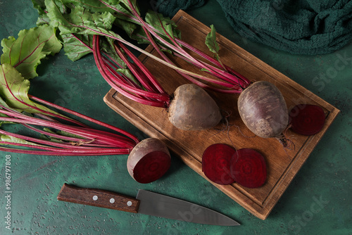 Cutting board with bunch of fresh cut beetroots and knife on green table photo