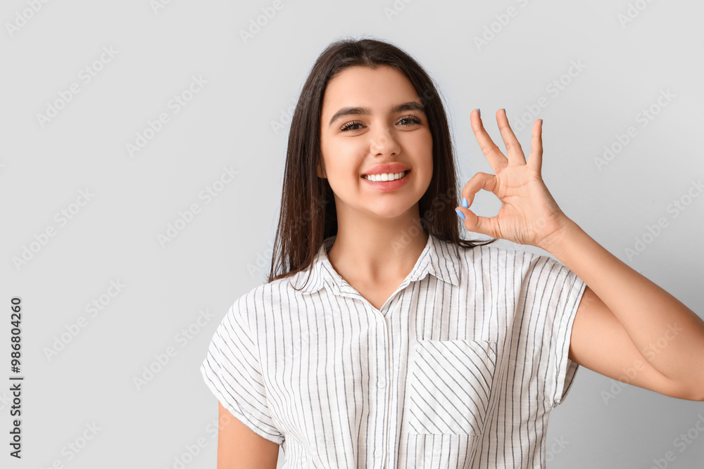 Smiling young woman with healthy teeth showing OK on light background Smiling young woman with healthy teeth showing OK on light background