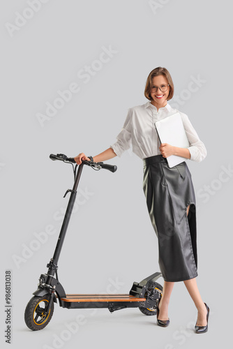 Happy young businesswoman with laptop and electric kick scooter on white background