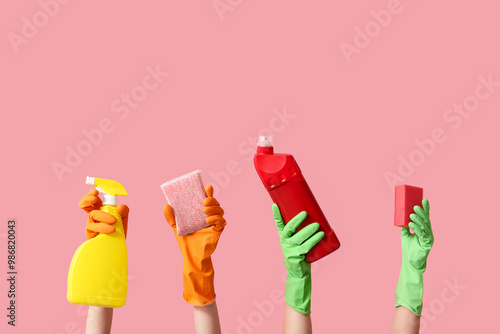 Female hands in rubber gloves with bottles of detergent and sponges on pink background