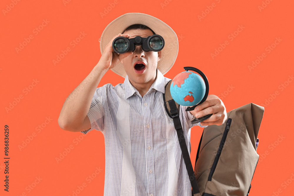 Shocked male tourist with globe looking through binoculars on orange background Shocked male tourist with globe looking through binoculars on orange background