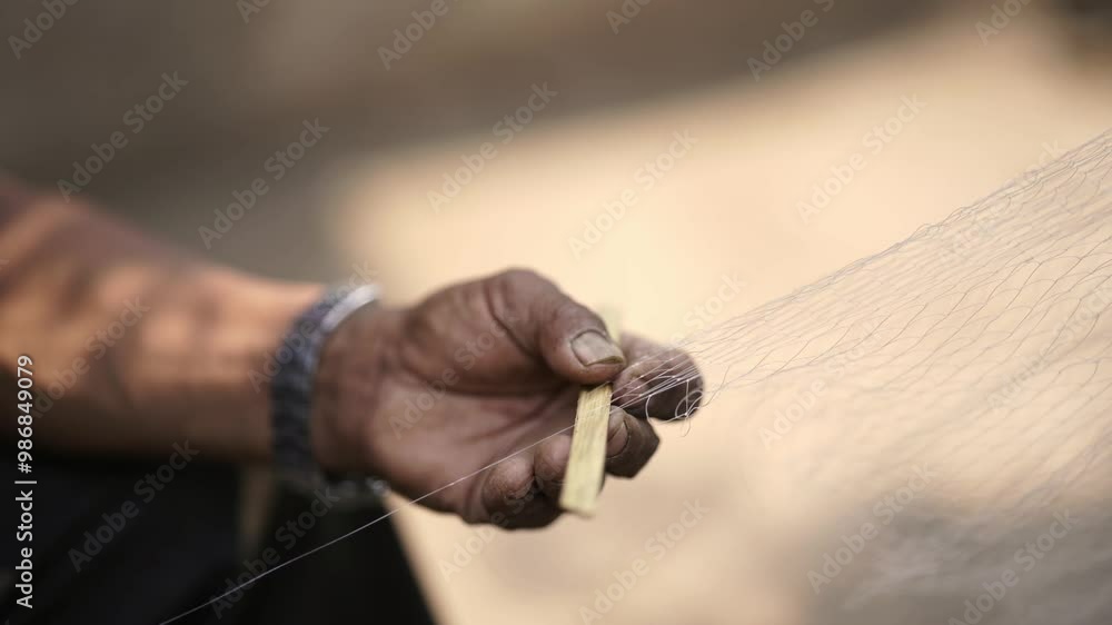 Close-up view of a man weaving a traditional fishing net by hand, using techniques from an Asian village in a Nepali rural setting Close-up view of a man weaving a traditional fishing net by hand, using techniques from an Asian village in a Nepali rural setting