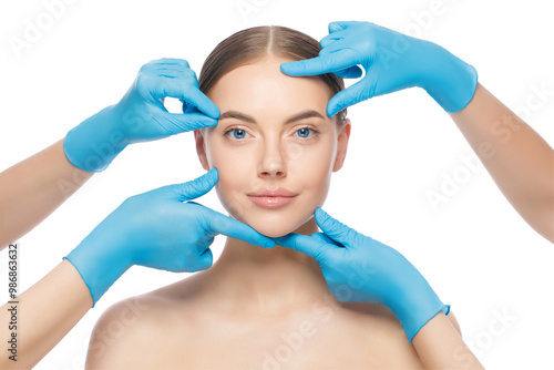 Portrait of young woman touched by doctors in blue gloves, preparing her for plastic surgery procedures