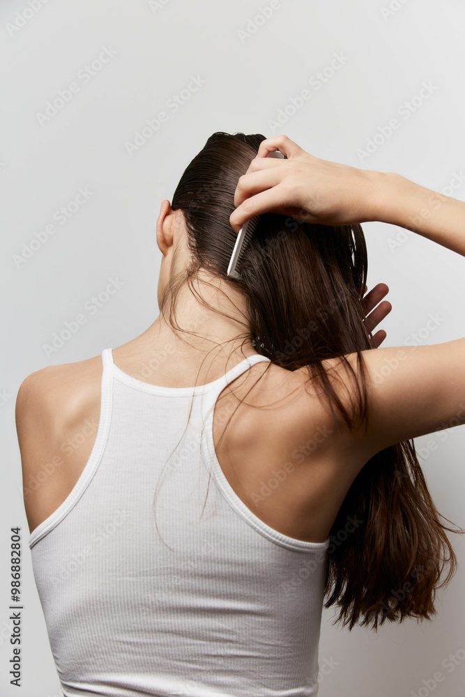 Hair care, grooming, beauty routine A young woman with long hair combs her hair while facing away from the camera, showcasing a simple and elegant look against a white background Hair care, grooming, beauty routine A young woman with long hair combs her hair while facing away from the camera, showcasing a simple and elegant look against a white background