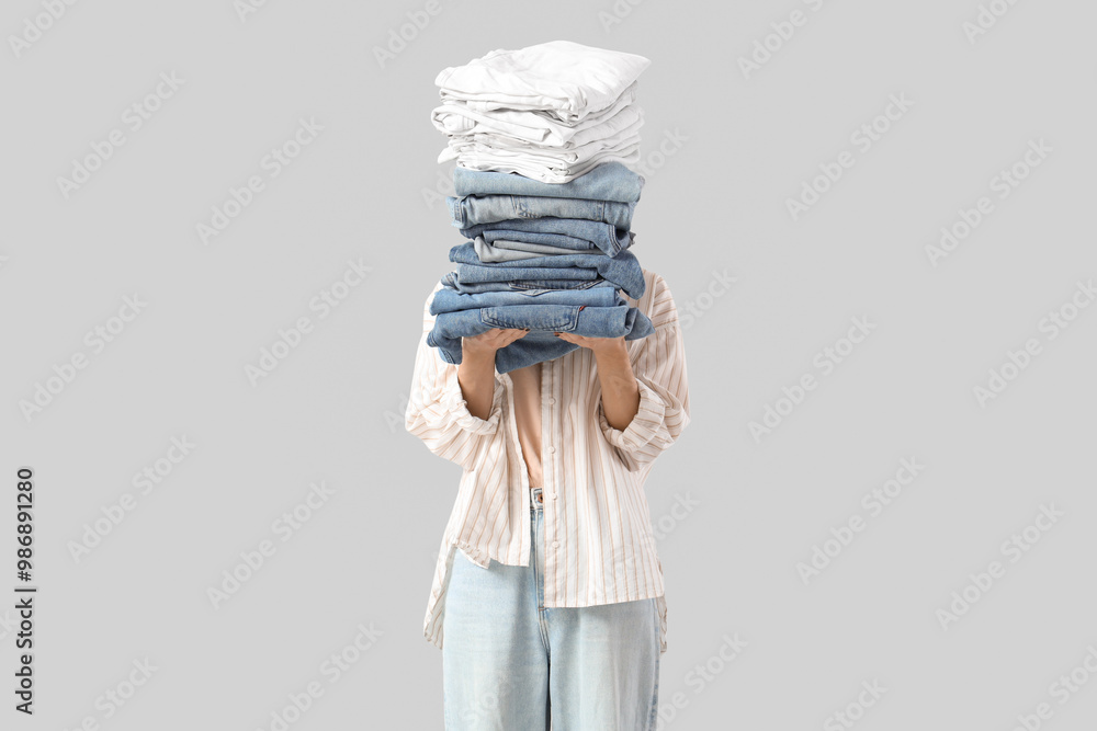 Naklejka premium Young woman with stack of clothes on light background