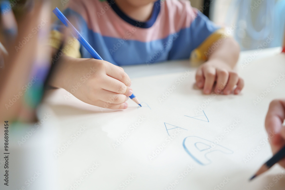 Closeup Asian young boy is drawing on a paper with a colored pencil with his mother at home. Closeup Asian young boy is drawing on a paper with a colored pencil with his mother at home.