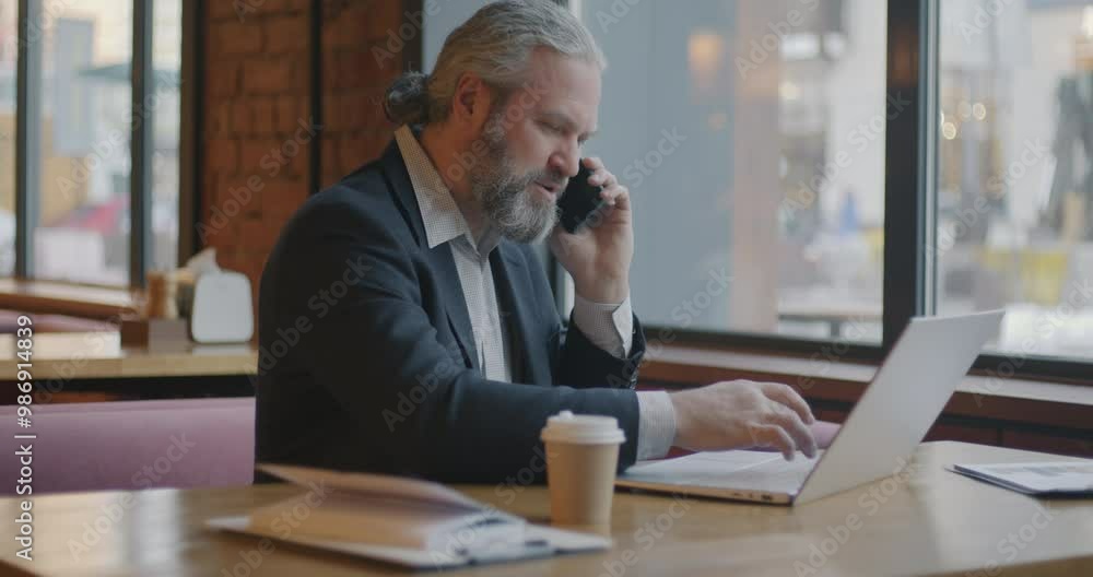 Male entrepreneur working with laptop and discussing business on mobile phone indoors in cafe. Professional communication and businessman concept. Male entrepreneur working with laptop and discussing business on mobile phone indoors in cafe. Professional communication and businessman concept.