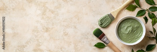 A flat lay of a bowl of green beauty mask, two brushes, and green leaves on a beige background. The image evokes a sense of natural beauty, relaxation, and self-care. It symbolizes the connection betw photo