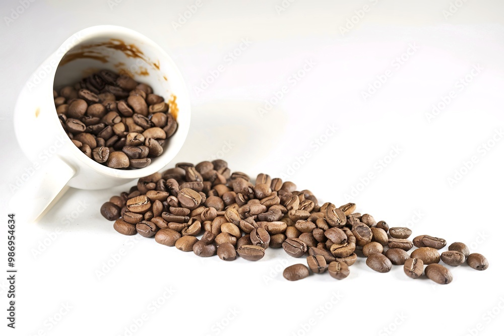 Spilled coffee beans from the white ceramic cup on white background Spilled coffee beans from the white ceramic cup on white background